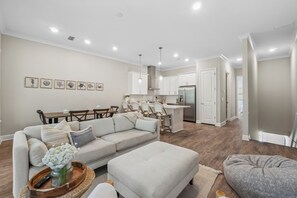 Een moderne woonkamer met een bank, een poef en een eethoek met stoelen en een tafel.