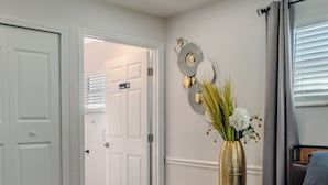 Quarto com uma cama grande, um ventilador de teto, um vaso com flores e uma porta que dá para outro cômodo.