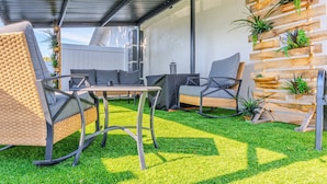 Um pátio externo com mobiliário de vime, uma mesa e um painel de plantas em madeira.