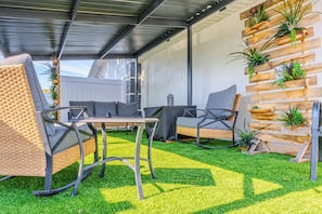 Een terras buiten met rieten meubels, een tafel en een plantenmuur van hout met planten.