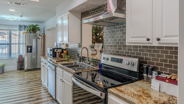 Uma cozinha moderna com eletrodomésticos de aço inoxidável, bancada de granito e painel de azulejos.