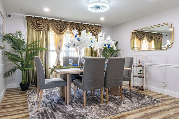 A dining area with a table set for four, surrounded by chairs, a large mirror, and a potted plant.