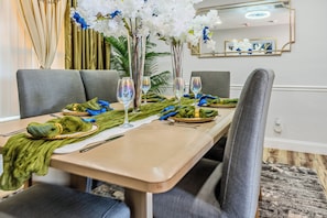 Een eettafel gedekt met groene servetten, bestek en wijnglazen, omringd door grijze gestoffeerde stoelen.