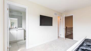 Un pasillo amplio con un baño a la izquierda, un televisor de pantalla plana montado en la pared y una escalera que sube a otro nivel.