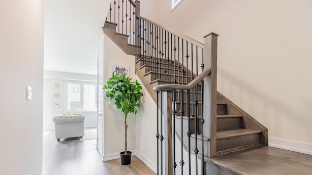 Una escalera con acabado de madera y barandillas negras que conduce a un rellano con una planta en maceta.