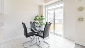 Un comedor con una mesa de vidrio y sillas negras, una planta en maceta y vista a un patio trasero a través de un ventanal corredero.