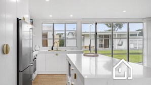 Een moderne keuken met witte kasten, een roestvrijstalen koelkast en een groot raam met uitzicht op de achtertuin.