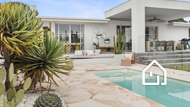 Een modern huis met een zwembad, terras en een tuin vol met cactussen.