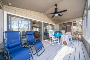 A covered outdoor area with blue lounge chairs, a table with a floral tablecloth, and a ceiling fan.