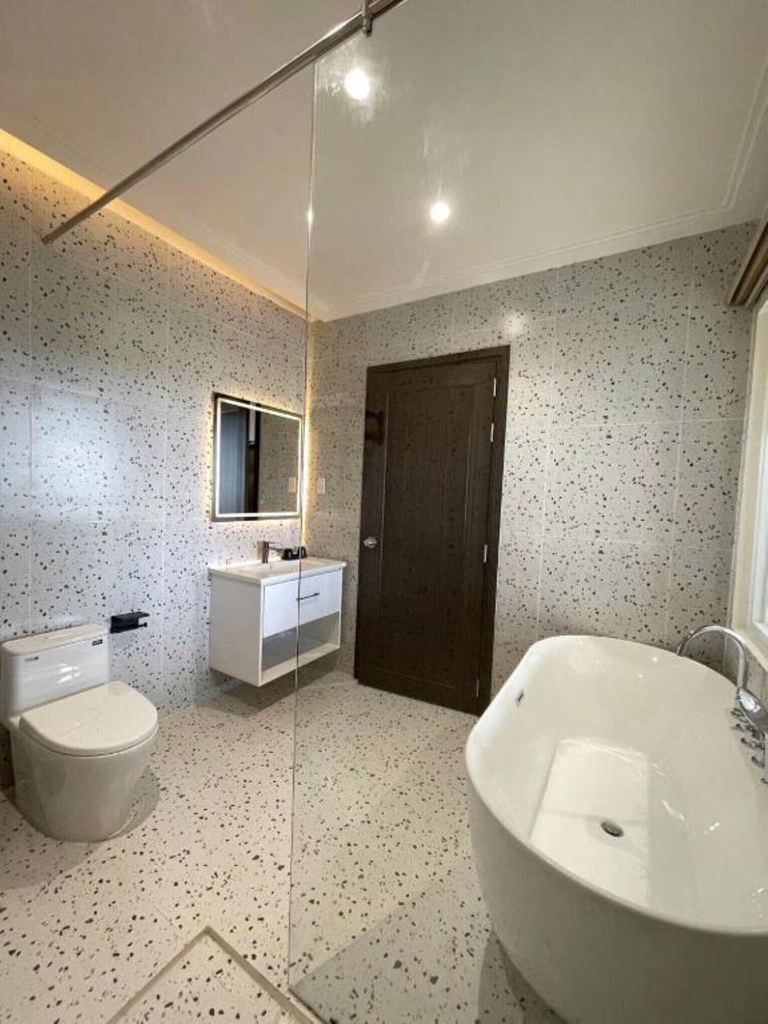 A modern bathroom with a freestanding bathtub, a toilet, and a vanity with a mirror.