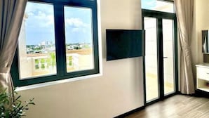 Una habitación de hotel con un ventanal grande, un televisor de pantalla plana montado en la pared y una puerta corrediza de vidrio que da a un espacio al aire libre.