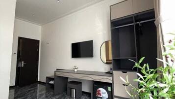 Habitación de hotel moderna con suelo de mármol, televisor de pantalla plana en la pared, un escritorio pequeño con silla y una planta en maceta.