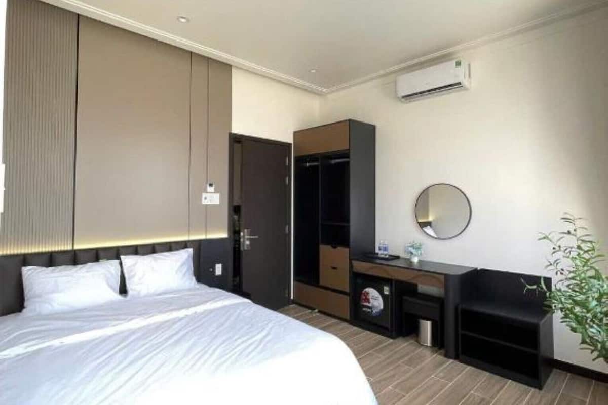 A hotel room with a bed, a wardrobe, a desk with a mirror, and an air conditioning unit.
