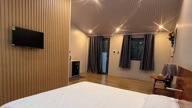 Una habitación de hotel con una cama grande, un televisor de pantalla plana montado en la pared, un escritorio con una lámpara y una ventana con cortinas.