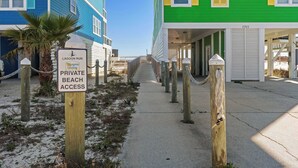 Een bordje voor privéstrandtoegang, een betonnen pad en twee kleurrijke strandhuizen.
