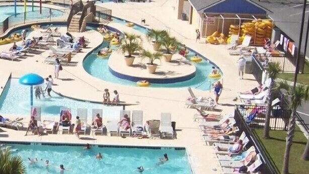 Un área de piscina con varias piscinas, sillones de descanso y un tobogán de agua.