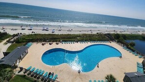 Un hotel frente a la playa con una amplia piscina, sillas de playa y vista al océano.