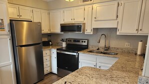 Una cocina moderna con armarios blancos, electrodomésticos de acero inoxidable, encimeras de granito y una isla central.