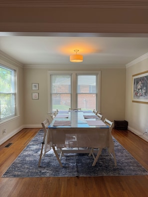A dining room with a rectangular table, white chairs, a blue rug, and a ceiling light. - Comfy Bungalow - 3bdrm, 2ba, 6 min to Downtown (Little Rock)