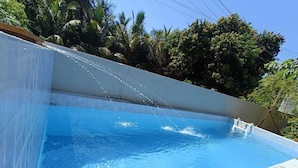 Une piscine à l’eau d’un bleu cristallin, entourée d’une végétation luxuriante et dotée d’une terrasse carrelée.