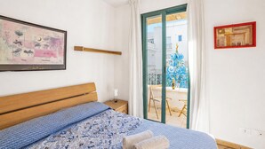 A bedroom with a bed, a nightstand, a window with a view of buildings, and artwork on the walls. - SeaEscape San Foca - Duplex with Sea-View Balcony, Melendugno, Italy (Melendugno)