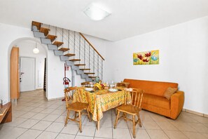 A dining area with a table set for four, a staircase, an orange sofa, and a painting on the wall. - SeaEscape San Foca - Duplex with Sea-View Balcony, Melendugno, Italy (Melendugno)