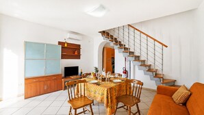 A dining area with a table set for four, a sofa, and a staircase. - SeaEscape San Foca - Duplex with Sea-View Balcony, Melendugno, Italy (Melendugno)