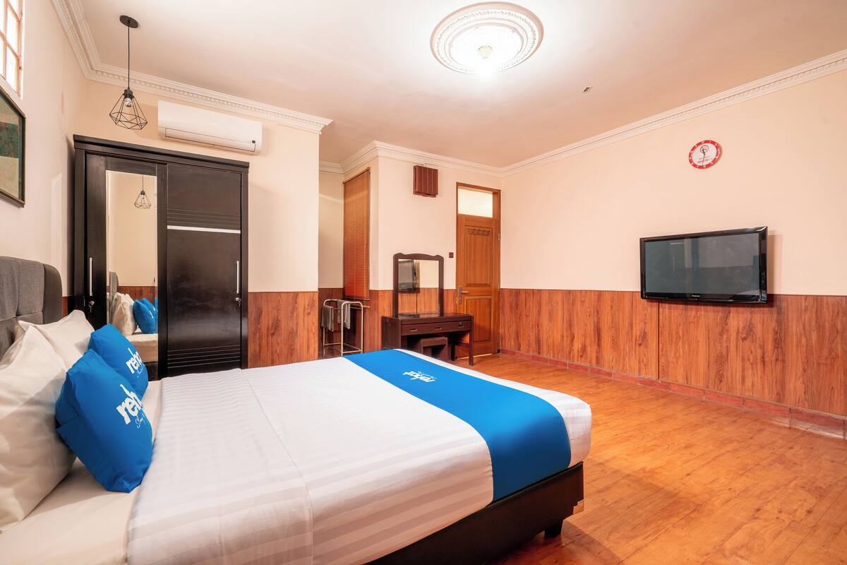 A hotel room with a bed, a television, a mirror, and a wooden floor.