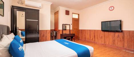 A hotel room with a bed, a television, a mirror, and a wooden floor.