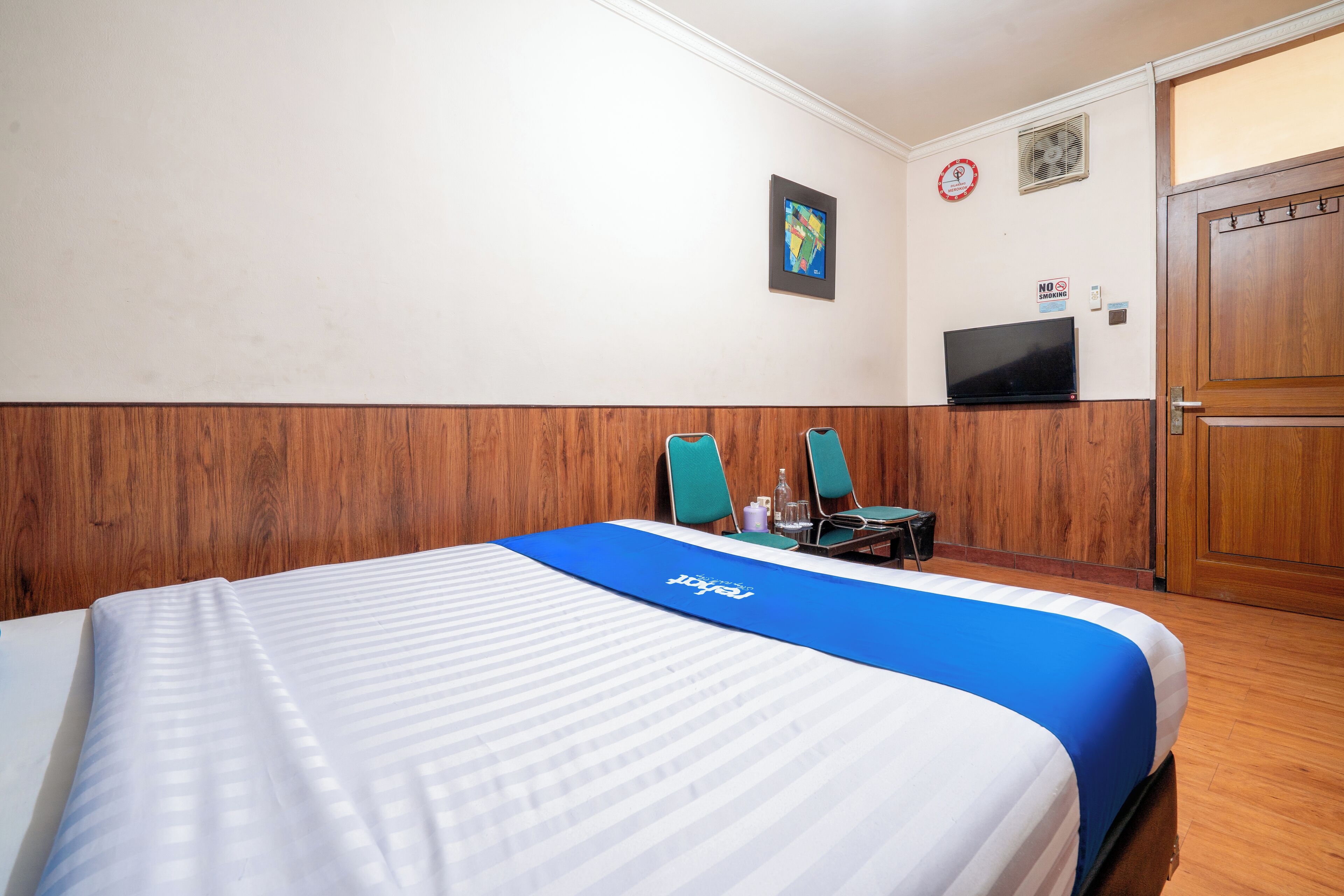 A hotel room with a bed, two chairs, a television, and a wooden door.