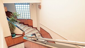 Un escalier avec des marches en bois et des rampes en métal, menant à un palier agrémenté d’un pot de fleurs et d’une fenêtre à croisillons.