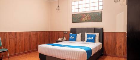 A hotel room with a wooden floor, a bed with a blue and white bedspread, a gray headboard, and a painting on the wall.