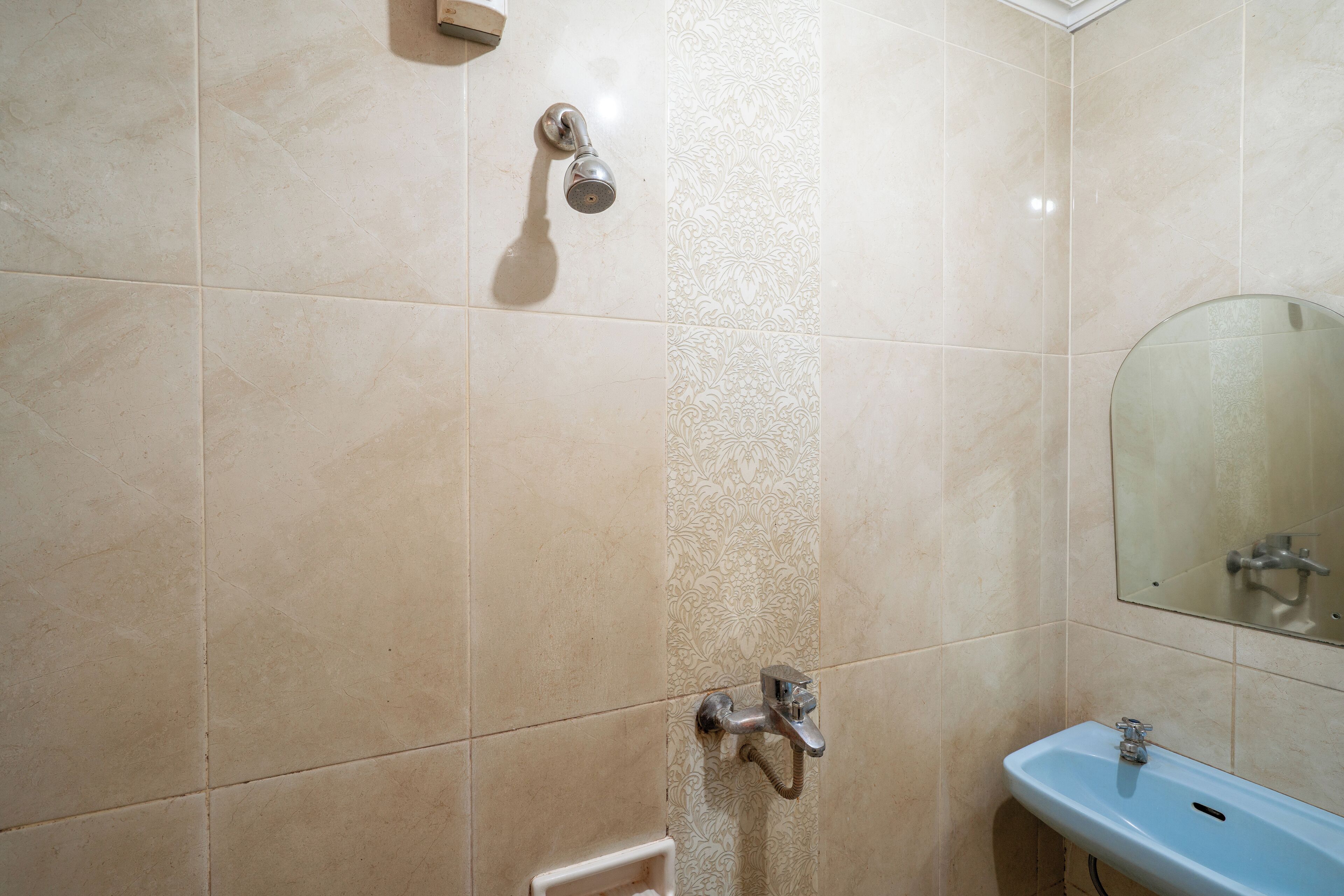 A bathroom with beige tiles, a shower, a sink, and a mirror.