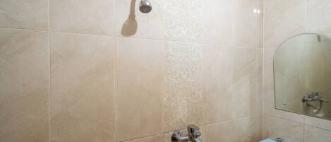 A bathroom with beige tiles, a shower, a sink, and a mirror.