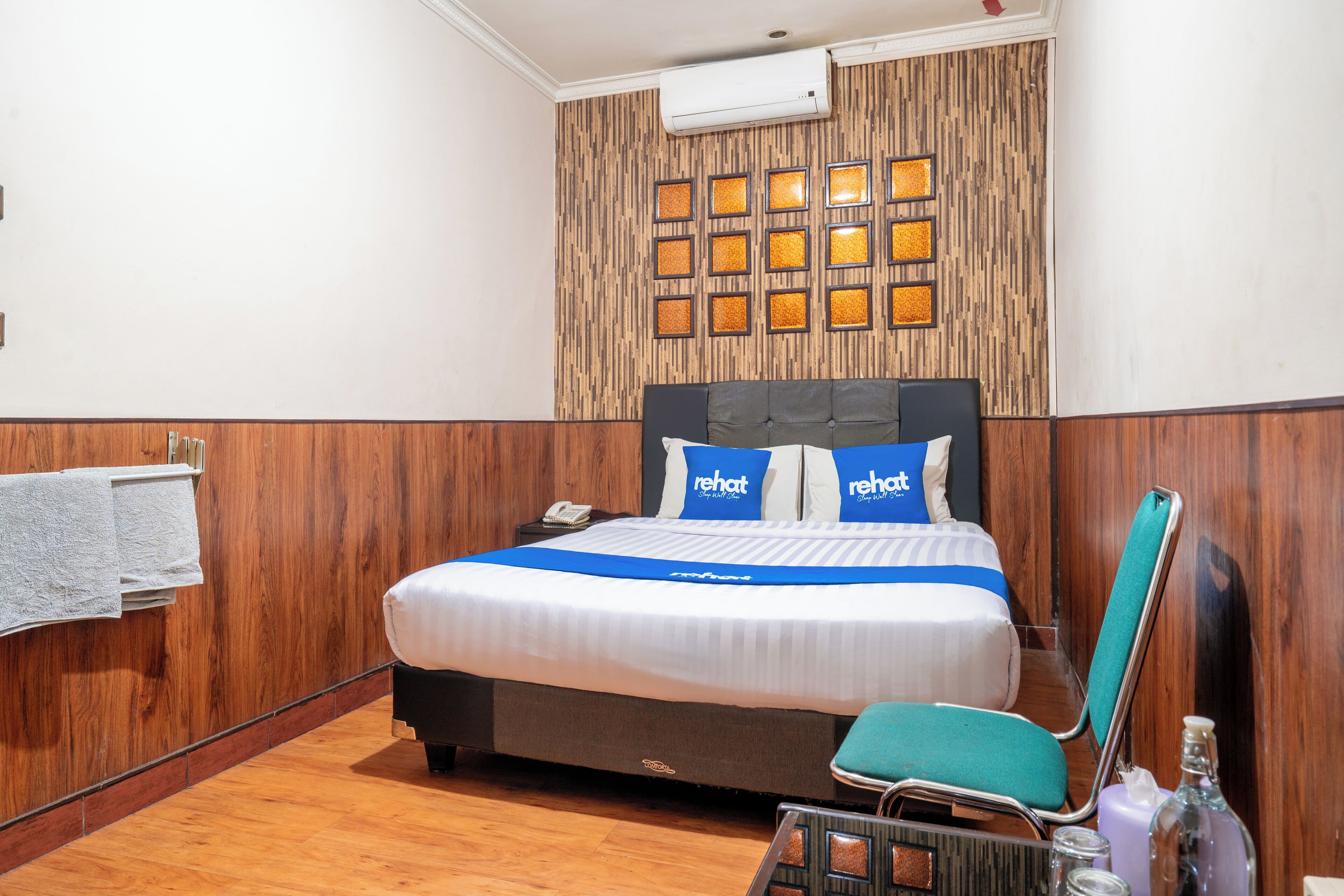 A hotel room with a wooden panel wall, a bed with a blue bedspread, and a chair.