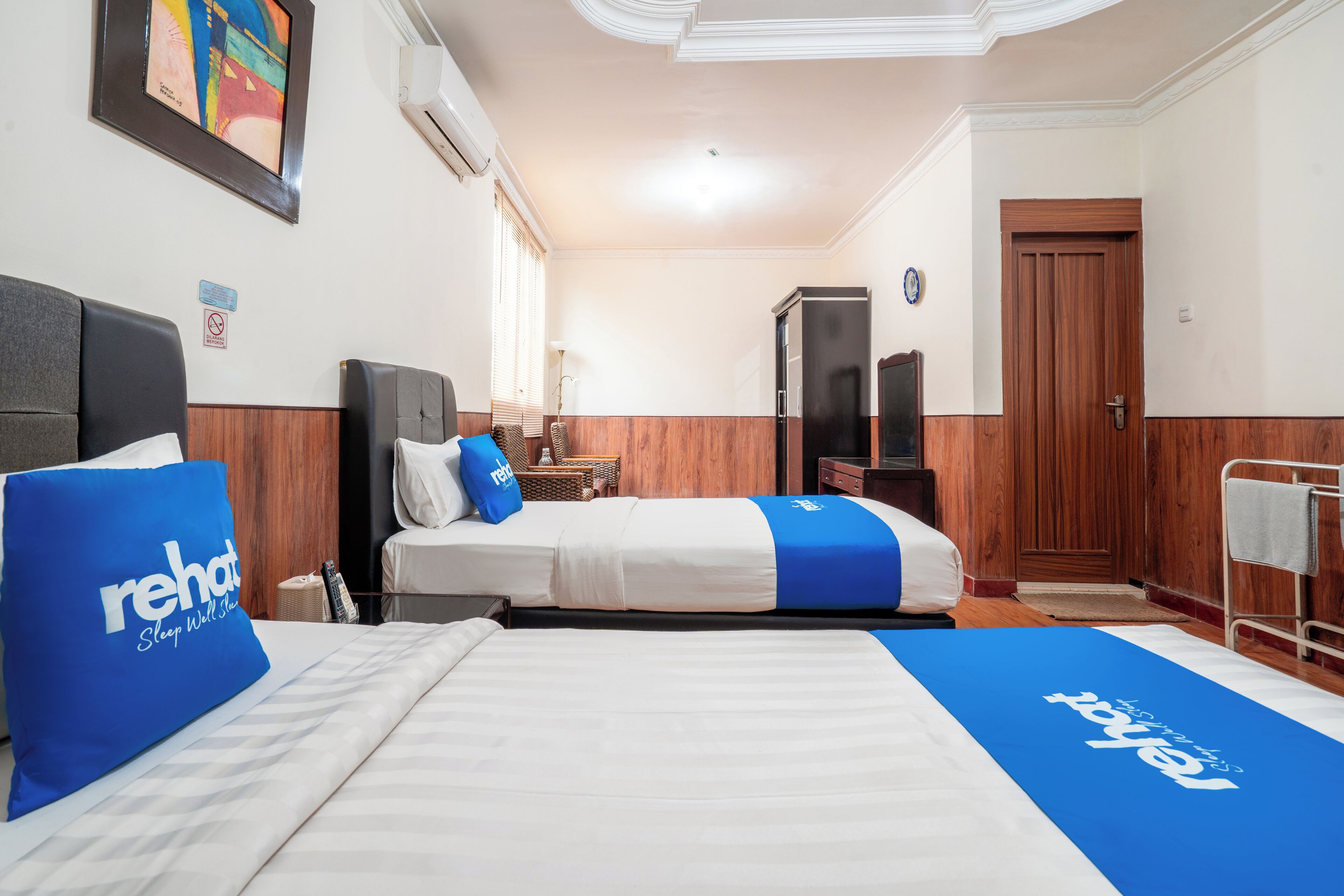 A hotel room with two beds, a wooden wardrobe, a television, and a framed picture on the wall.