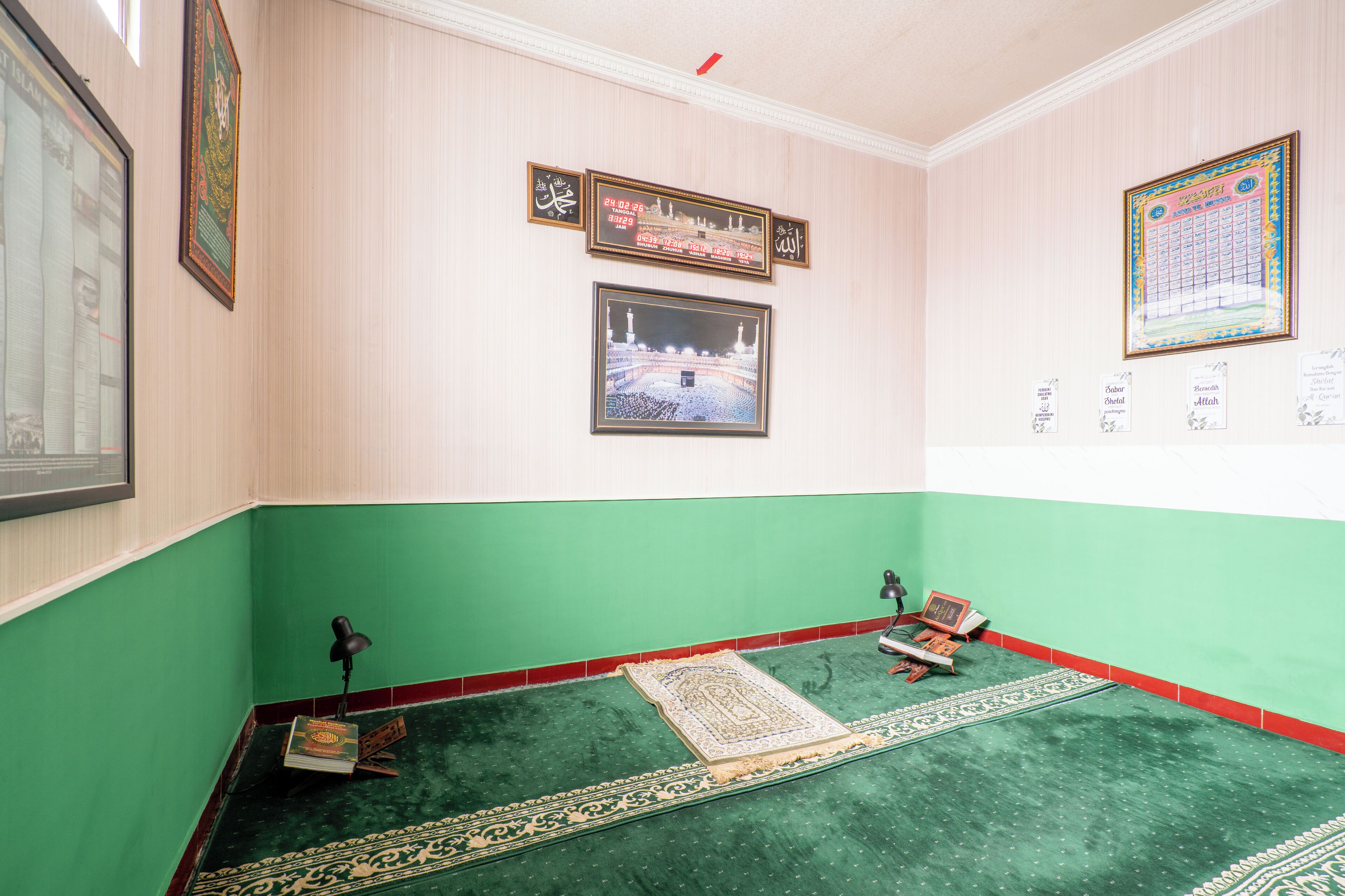 A prayer room with a green carpet, a prayer mat, a prayer rug, and a framed picture of a mosque.