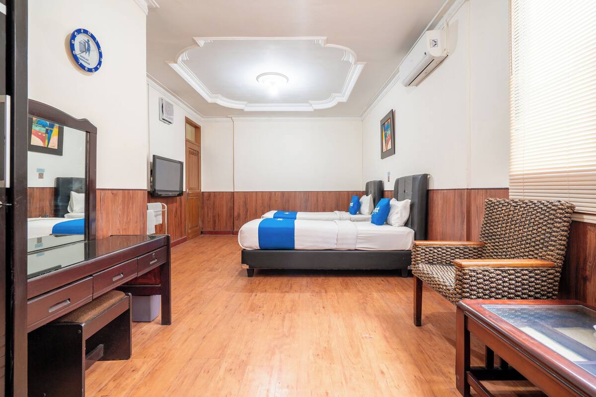 A hotel room with a bed, a desk, a chair, a television, and a clock on the wall.