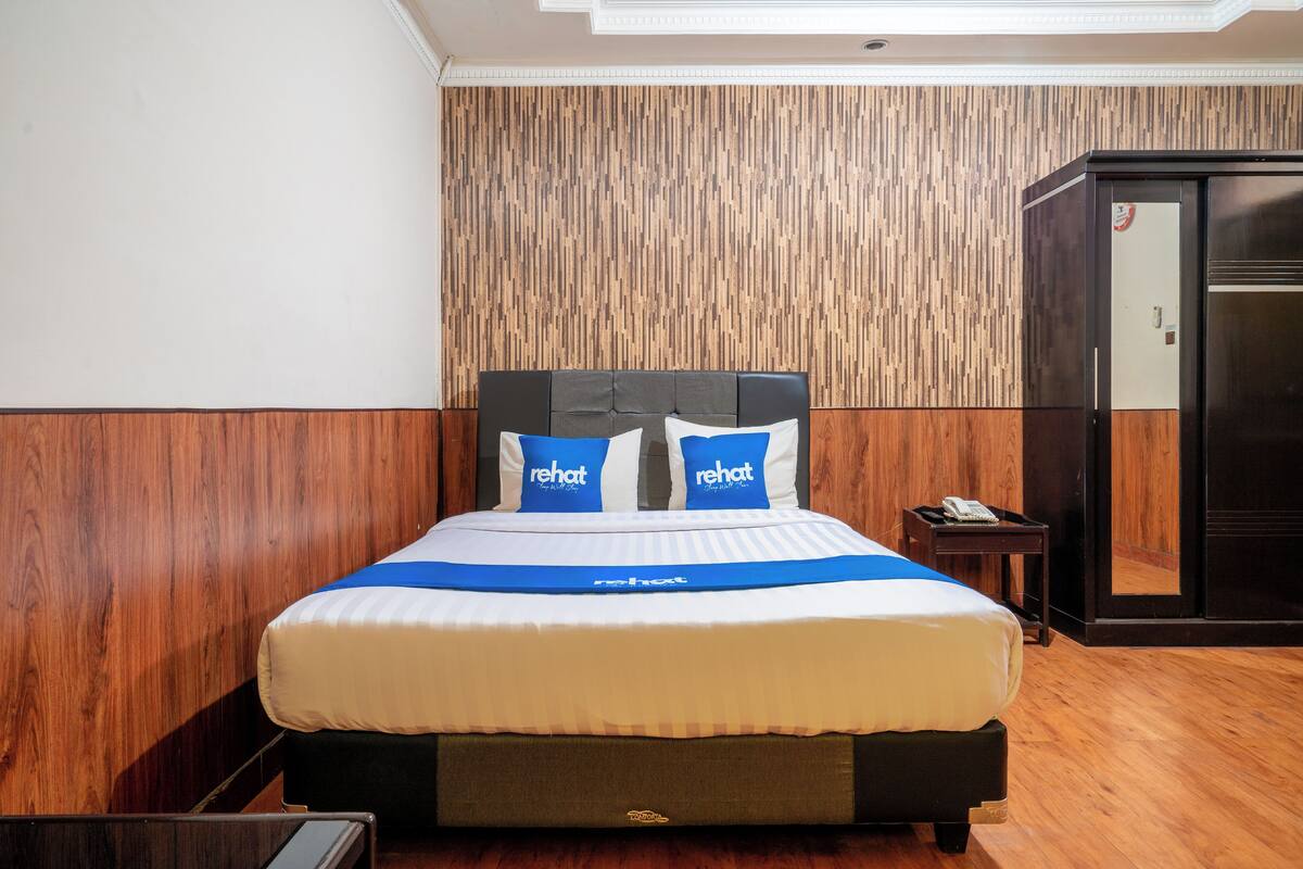 A hotel room with a bed, wooden panel wall, and a minibar.