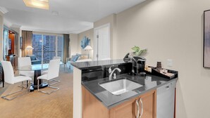 A modern kitchen with a black countertop, stainless steel sink, and a coffee machine. There is a dining area with a glass table and white chairs. - Corner Suite with Strip View, F1, Balcony at MGM Signature, NO Resort Fee - 1621 (Las Vegas)