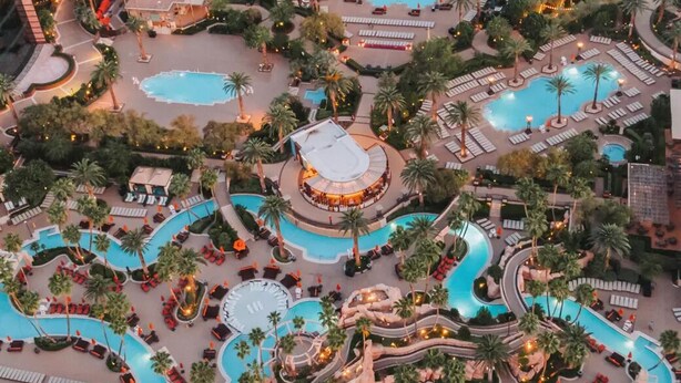 An aerial view of a resort with multiple swimming pools, palm trees, and lounge areas. - Corner Suite with Strip View, F1, Balcony at MGM Signature, NO Resort Fee - 1621 (Las Vegas)