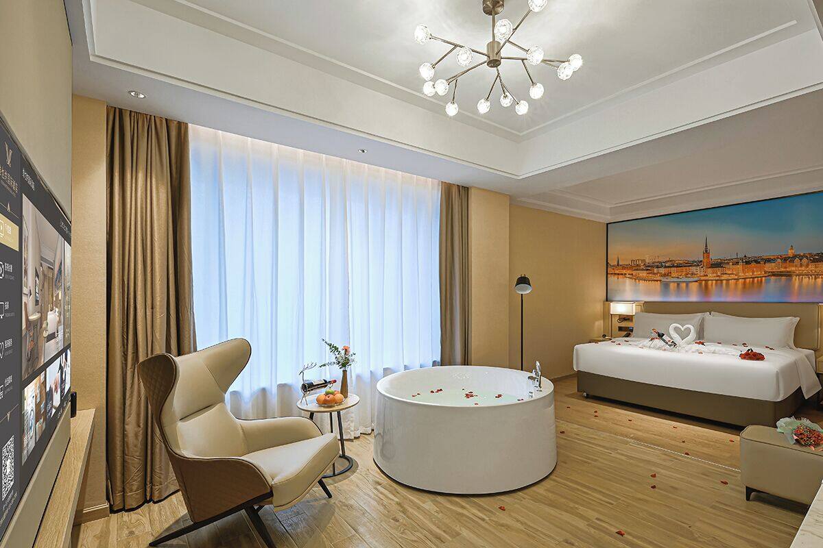 Ein Hotelzimmer mit einem großen Bett, einer runden Badewanne, einer Sitzecke mit Sessel und Tisch und Blick auf die Stadt.
