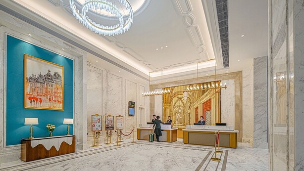 Een hotel lobby met marmeren vloeren, een receptiebalie, een grote kroonluchter en een stadsgezichtschilderij in een lijst.