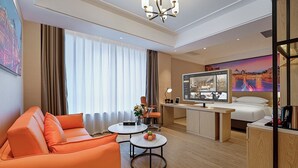 Hotelkamer met een bank, bureau, bed, televisie en een groot raam met gordijnen.