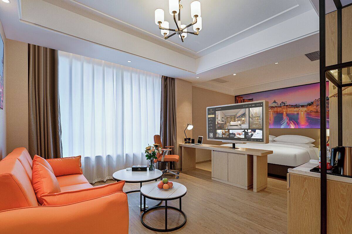Ein Hotelzimmer mit einer Sitzecke, einem Schreibtisch, einem Bett, einem Fernseher und einem großen Fenster mit Vorhängen.