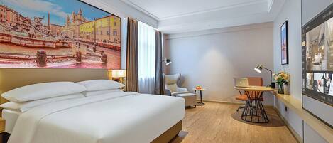 A hotel room with a large bed, a desk with a chair, a small table with a lamp, and a painting of a cityscape on the wall.