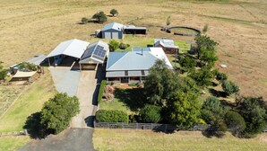 A large, modern farmhouse with multiple buildings, including a main house with a large garage and solar panels, surrounded by expansive fields and sparse trees. - Leisurely Long Swamp Retreat - 3 Bed, 2 Bath (Forest Reefs)