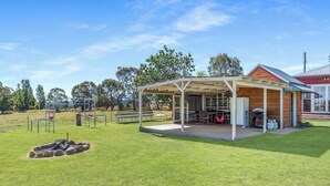 A covered outdoor area with a barbecue and seating, surrounded by a grassy field and trees. - Leisurely Long Swamp Retreat - 3 Bed, 2 Bath (Forest Reefs)