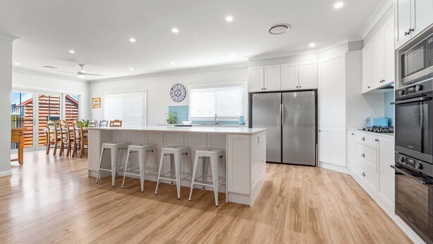 A modern kitchen with white cabinets, a stainless steel refrigerator, a double oven, and a bar area with stools. - Leisurely Long Swamp Retreat - 3 Bed, 2 Bath (Forest Reefs)