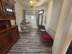 Una habitación con una silla colgante, un banco, un aparador de madera y una ventana con persianas.